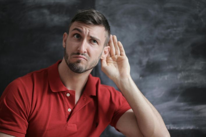 Thoughtful man listening intently against a chalkboard background in a red polo shirt.