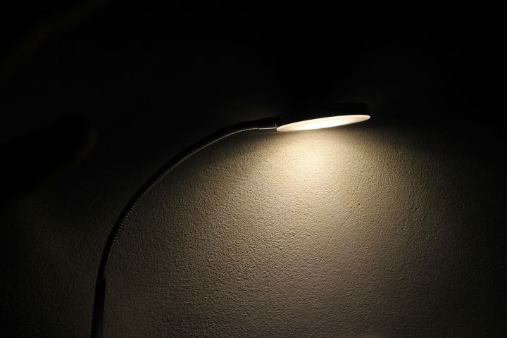 A sleek desk lamp casts a soft glow on a textured wall, creating a moody ambiance.