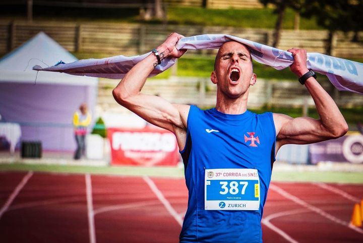 Athlete celebrates victory at marathon finish line triumphantly raising tape overhead.