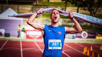 Athlete celebrates victory at marathon finish line triumphantly raising tape overhead.