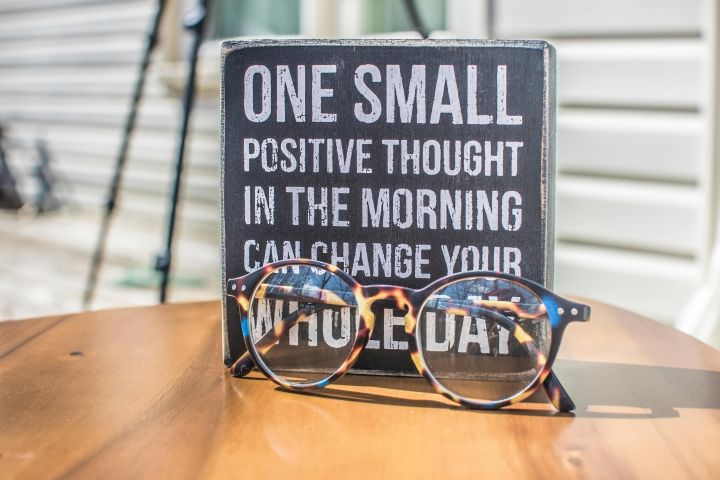 Eyeglasses resting on a table in front of a motivational quote sign, emphasizing positivity.