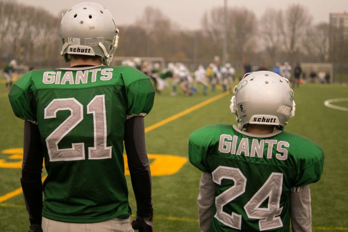 Two football players, wearing green Giants jerseys, preparing for a match on a field.