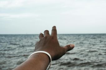 A hand reaching towards the horizon over the sea, signifying aspiration.