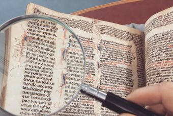 A hand holding a magnifying glass over an antique book page, revealing intricate text and design.
