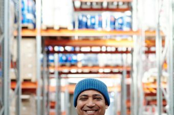 Happy warehouse worker smiling in a storeroom wearing a blue beanie and uniform.
