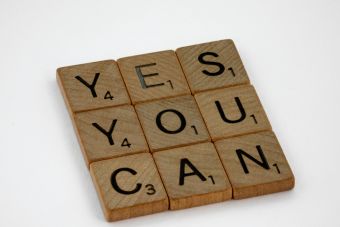 Wooden Scrabble tiles on white surface spelling 'Yes You Can,' promoting positivity and motivation.