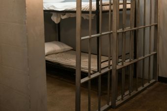 A prison cell featuring a metal bunk bed and striped sheets.