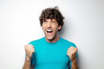 Portrait of a joyful man in a blue shirt celebrating with excitement and closed eyes.