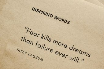 Motivational quote 'Fear kills more dreams than failure ever will.' by Suzy Kassem on paper texture.