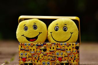 Two yellow smiley plush toys in an emoji-themed box, expressing fun and happiness.