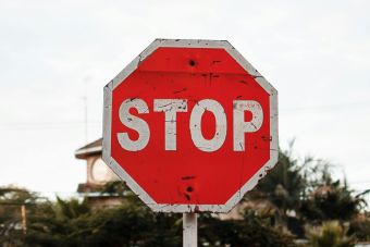 A prominent red stop sign on a city street amidst trees and buildings.