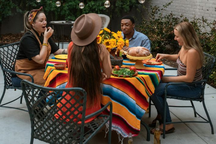 A diverse group of friends enjoying Mexican cuisine at an outdoor round table with colorful decor.