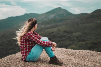 A woman in casual wear enjoys solitude on a scenic Brazilian mountain, embracing a moment of reflection.