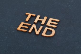 Wooden block letters spelling 'The End' on dark surface, artistic composition.