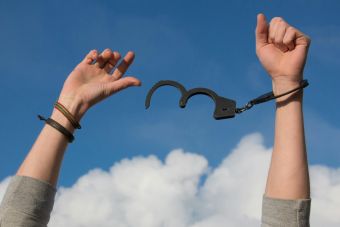 Symbolic image of freedom with open handcuffs against a bright blue sky.