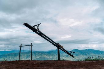 A rustic wooden seesaw in a rural hilltop setting under a cloudy sky.