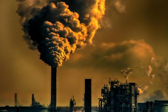 A factory emitting smoke clouds against a dark sunset sky, illustrating air pollution and industrial impact.