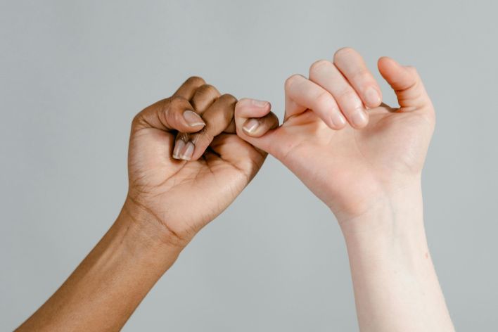 Two hands linking pinkies, symbolizing friendship and trust across ethnicities.