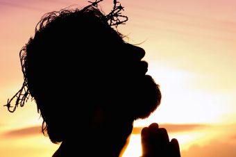 A silhouette of a man praying at sunset, wearing a crown of thorns, symbolizing faith and hope.
