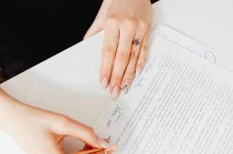 A woman's hands holding a pen over a paper document. Indoor writing scene.