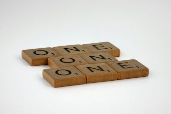 Scrabble tiles spelling 'ONE' arranged in an overlapping pattern on a plain background.