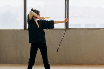 A determined young woman practicing archery indoors, showcasing focus and strength.