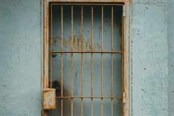 A weathered metal grilled door against a textured wall, capturing urban decay.