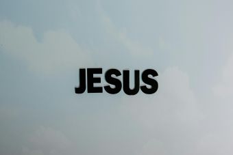 Minimalist image with bold 'JESUS' text against a cloudy sky background.