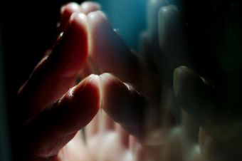 A hand pressing against a glass surface with vivid reflections, creating a moody atmosphere.