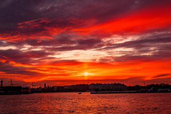 A stunning sunset paints the sky and harbor with vibrant reds and oranges, creating a scenic seascape.