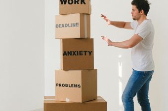 A man in casual attire balances boxes labeled with stress-related words indoors.