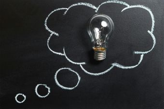 Light bulb laying on chalkboard with drawn thought bubble, symbolizing creative ideas.