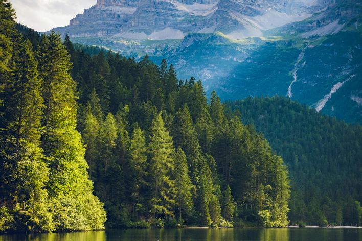 Peaceful alpine landscape featuring a serene lake with mountain and forest reflections.