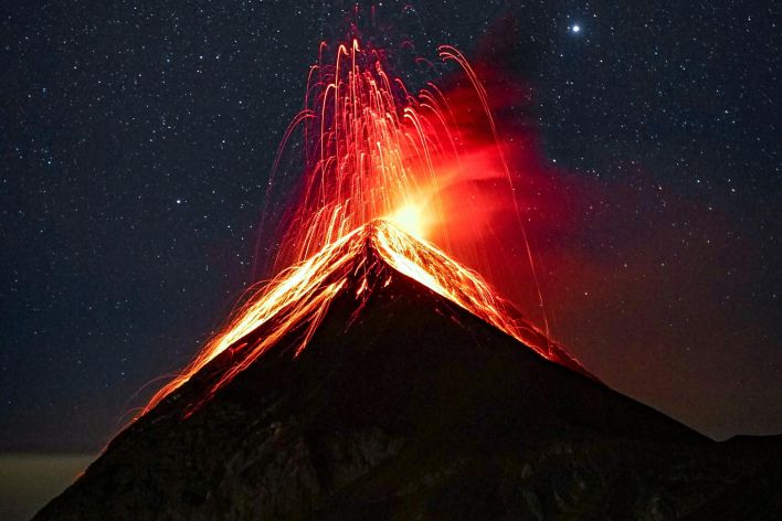 A breathtaking view of a volcano eruption with glowing lava against a starry night sky.
