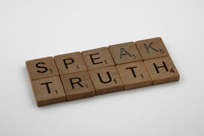 Wooden Scrabble tiles forming the words 'Speak Truth' on a white background.