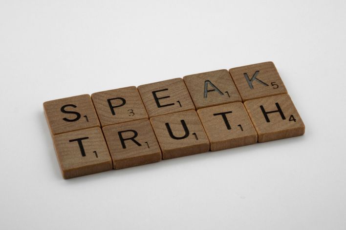 Wooden Scrabble tiles forming the words 'Speak Truth' on a white background.