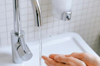 A woman washing hands under a faucet in a clean bathroom for hygiene.