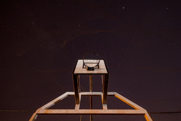 A low angle shot of a basketball hoop against a starry night sky.
