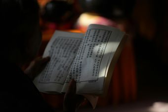 Close-up of hands holding a Chinese book, illuminated softly amidst shadows, emphasizing reading focus.