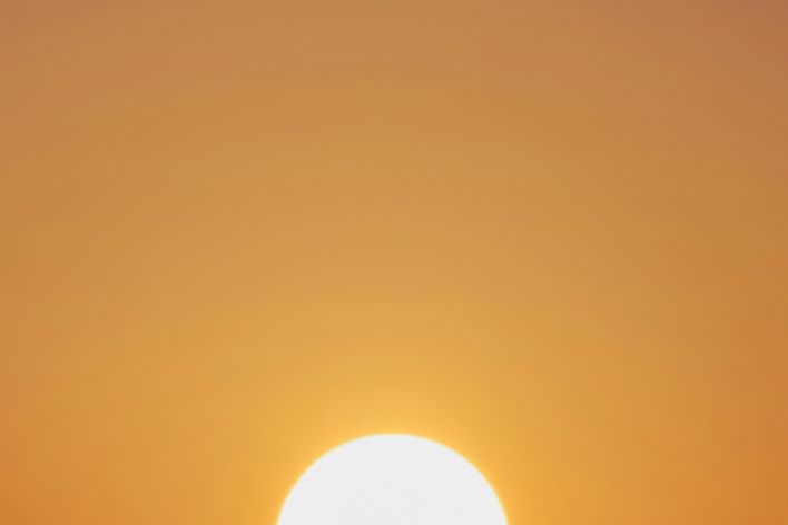 A vibrant sunset with a vivid orange sky and a prominently setting sun.