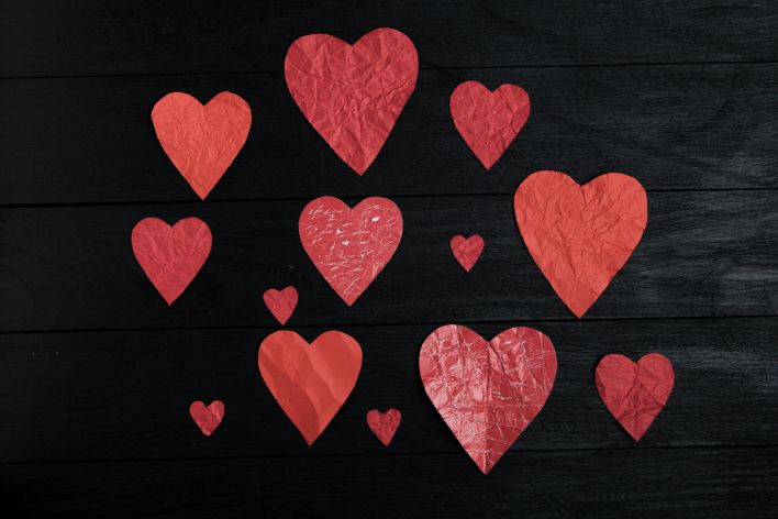 A collection of red paper hearts on a textured black wooden surface, perfect for Valentine's themes.